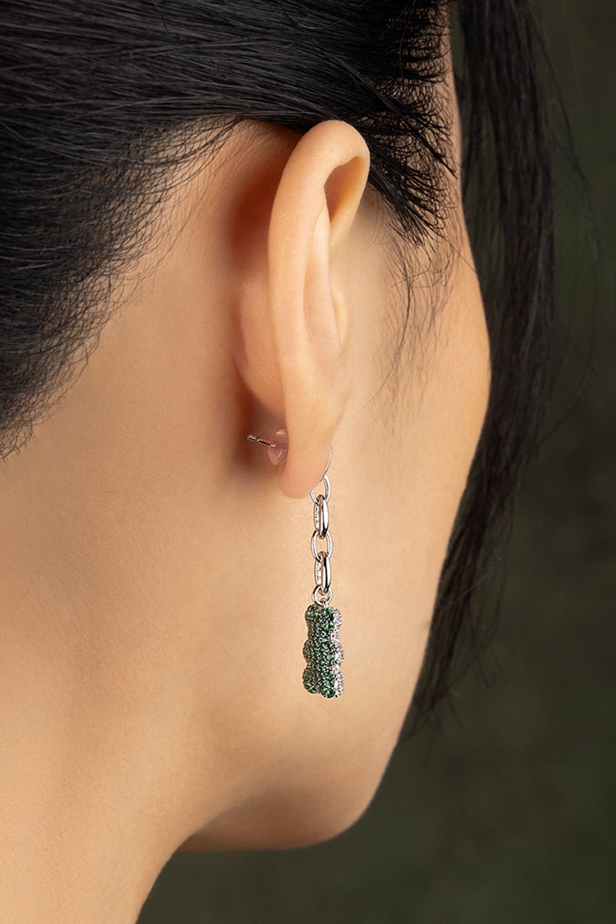 Close-up of an ear wearing a green stones earring with a blurred background