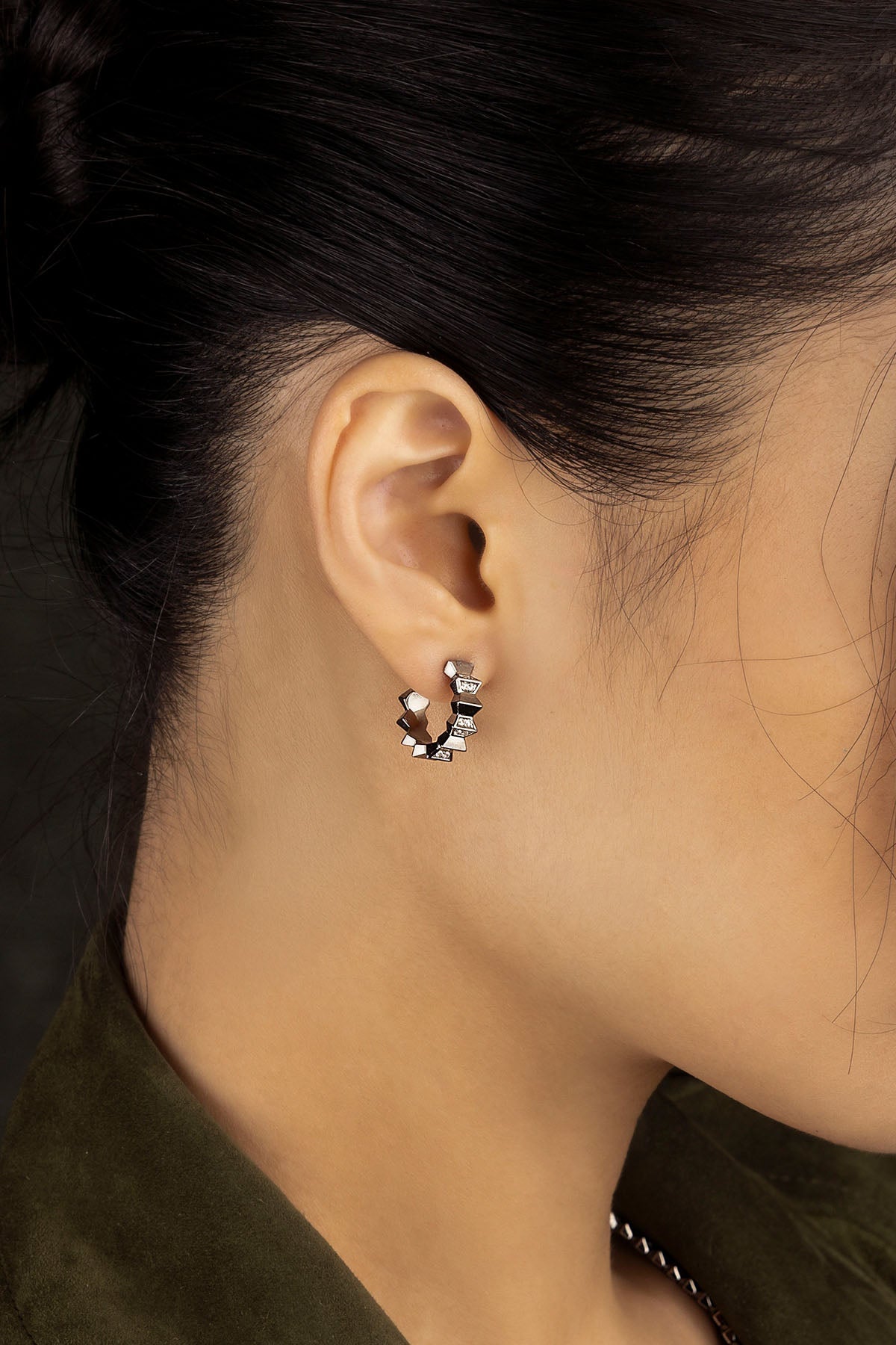 Close-up of an ear wearing a silver hoop earring with small stones.