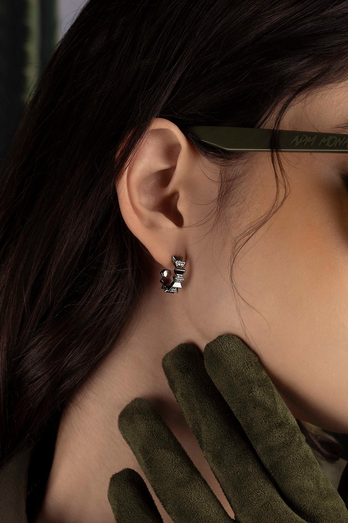 Close-up of an ear with a silver earring, wearing green gloves.