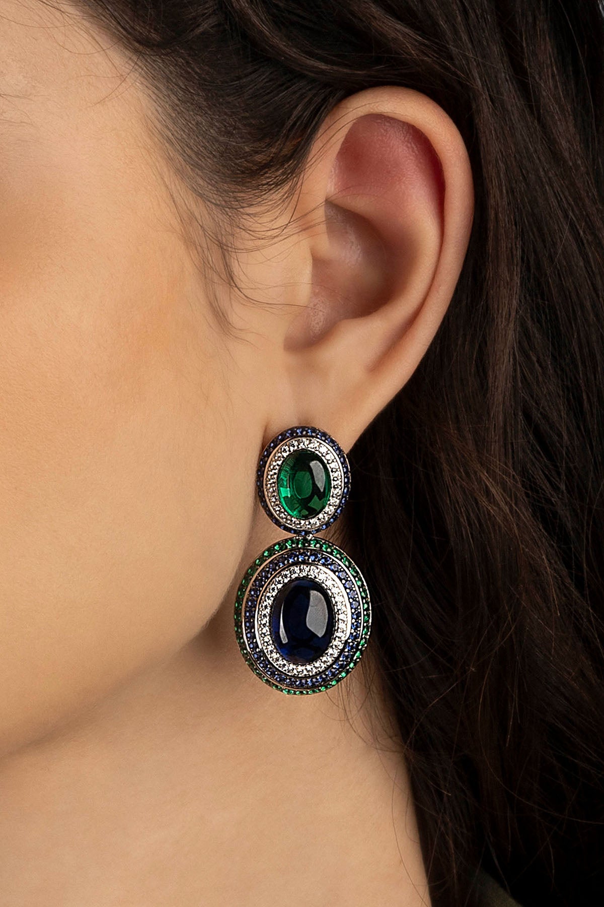 Close-up of a model wearing a earring with green and blue gemstones.