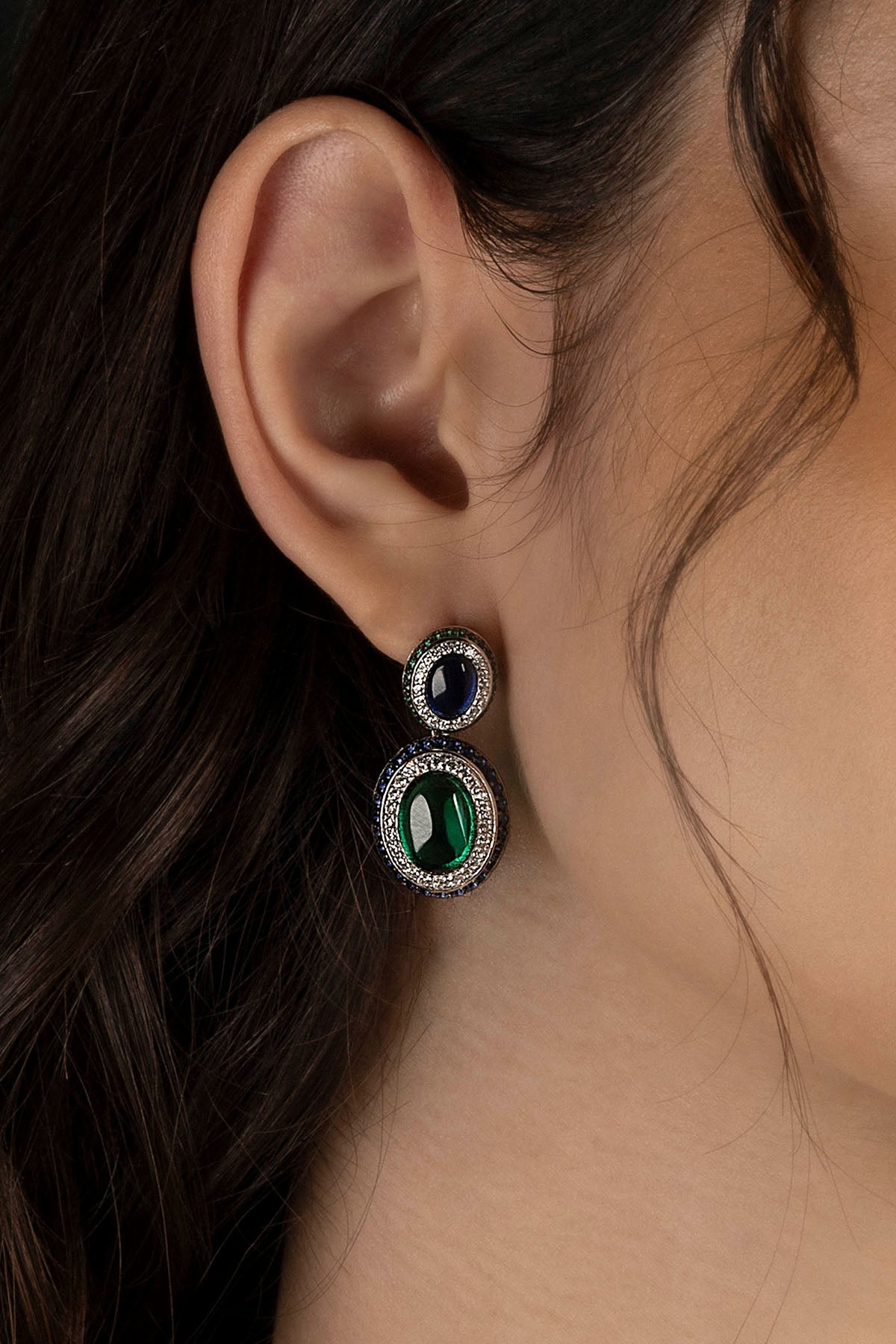 Close-up of an ear wearing a pair of green and blue stones earrings.