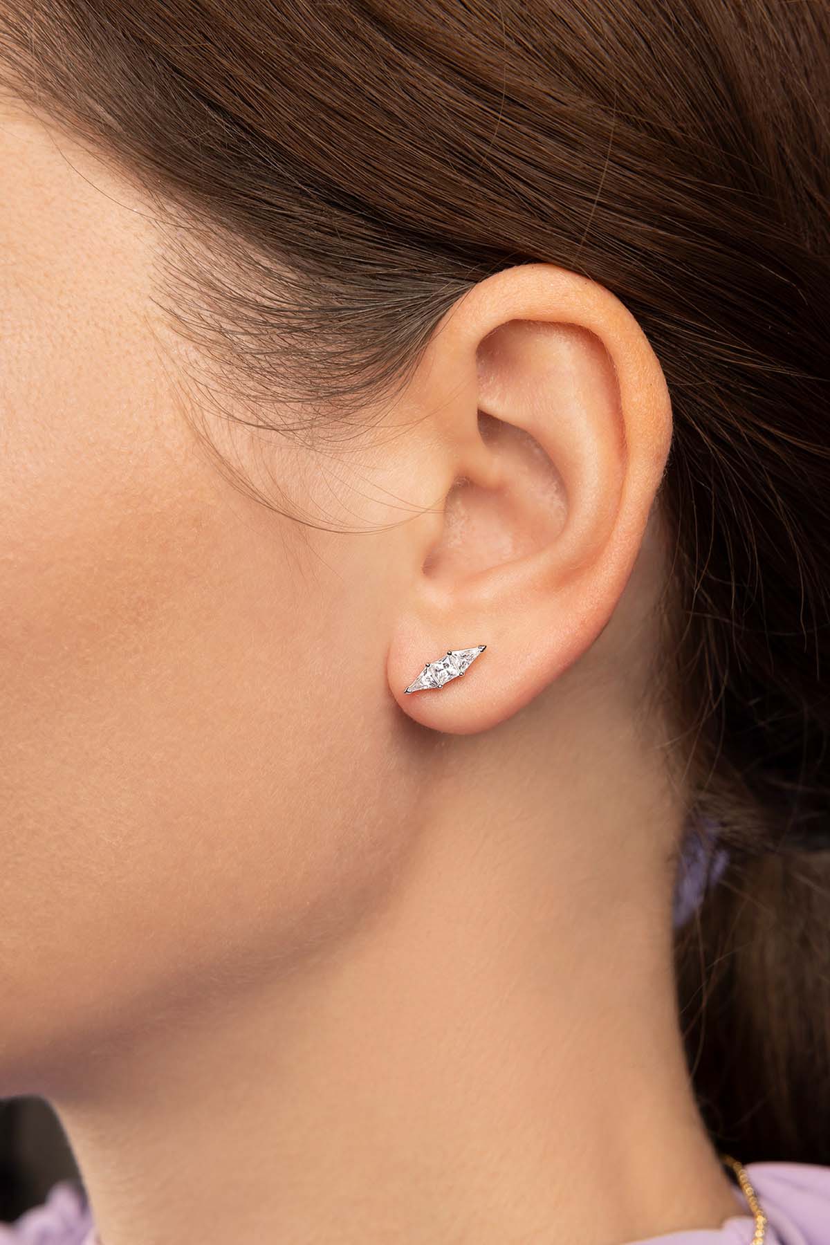 Close-up of an ear wearing a zirconia earring with purple background