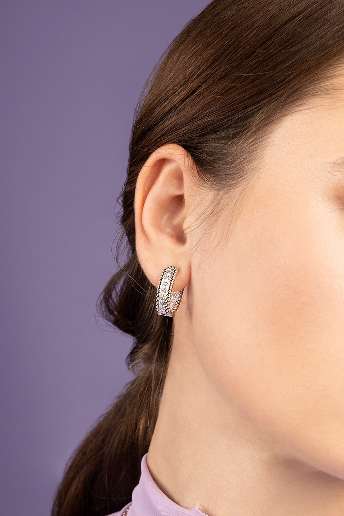 Close-up of a person wearing a silver earring against a purple background