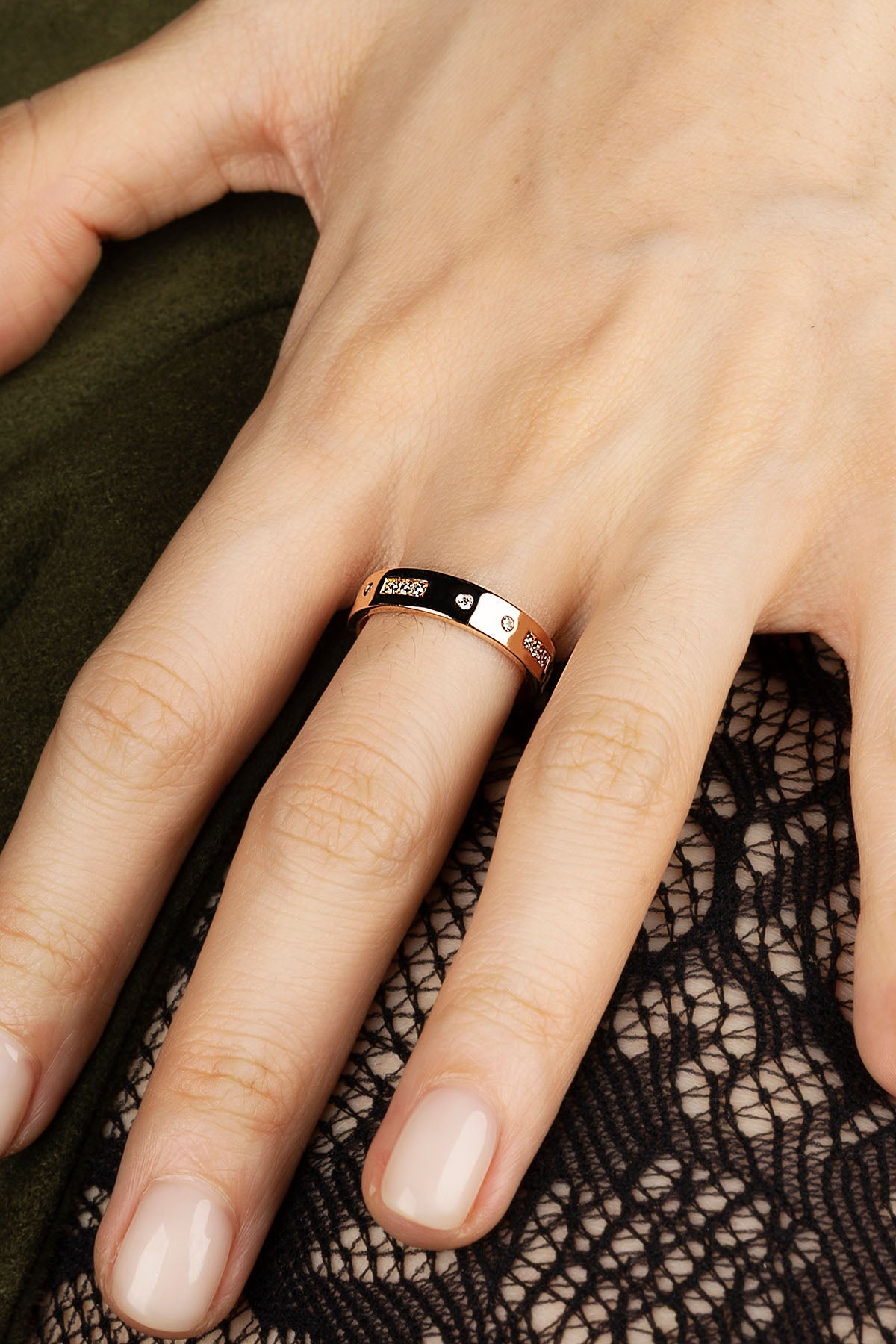 Close-up of a hand wearing a rose gold ring on a dark fabric background.