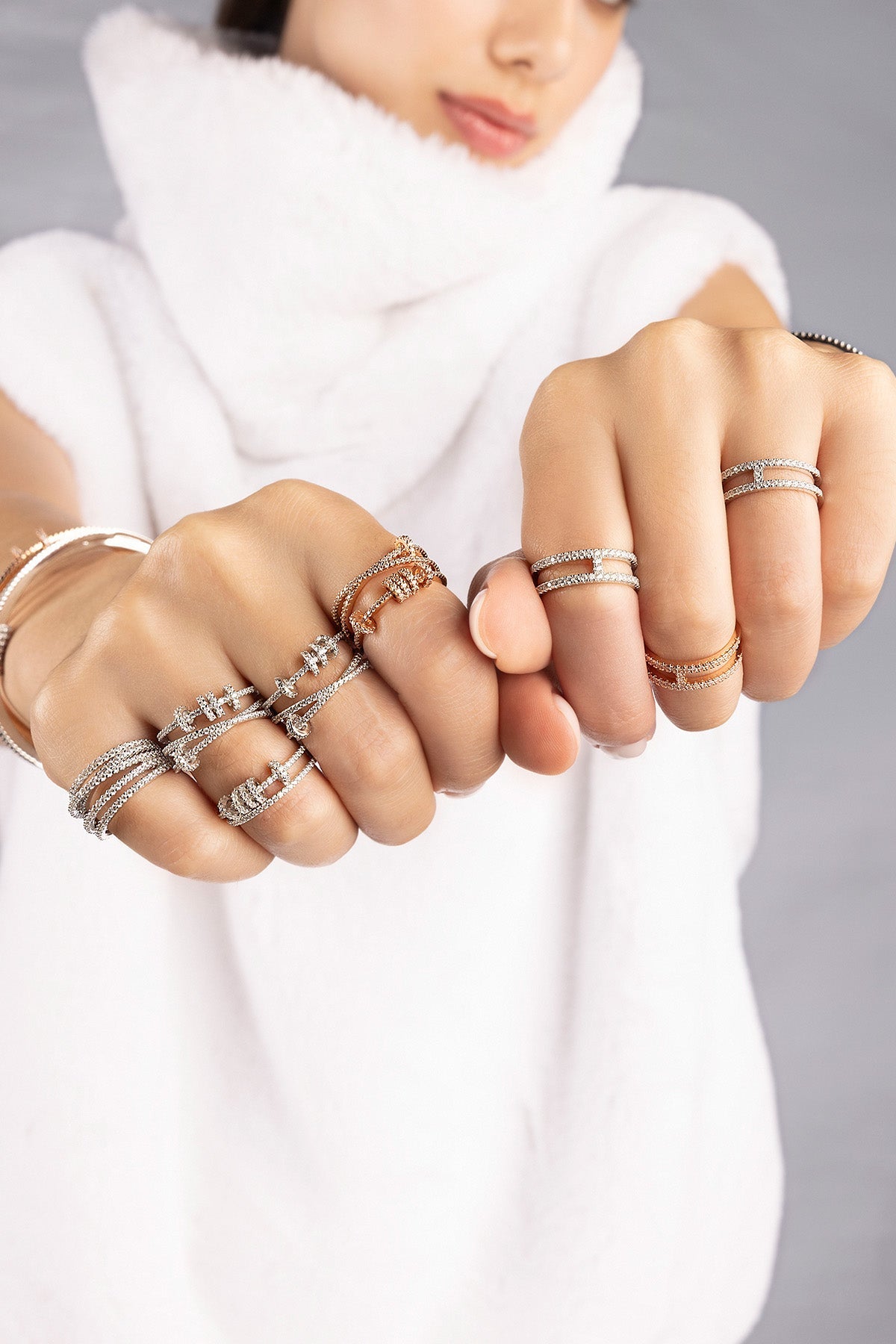 Close-up of hands wearing multiple APM MONACO rings with sliding-hoops design on a plain background