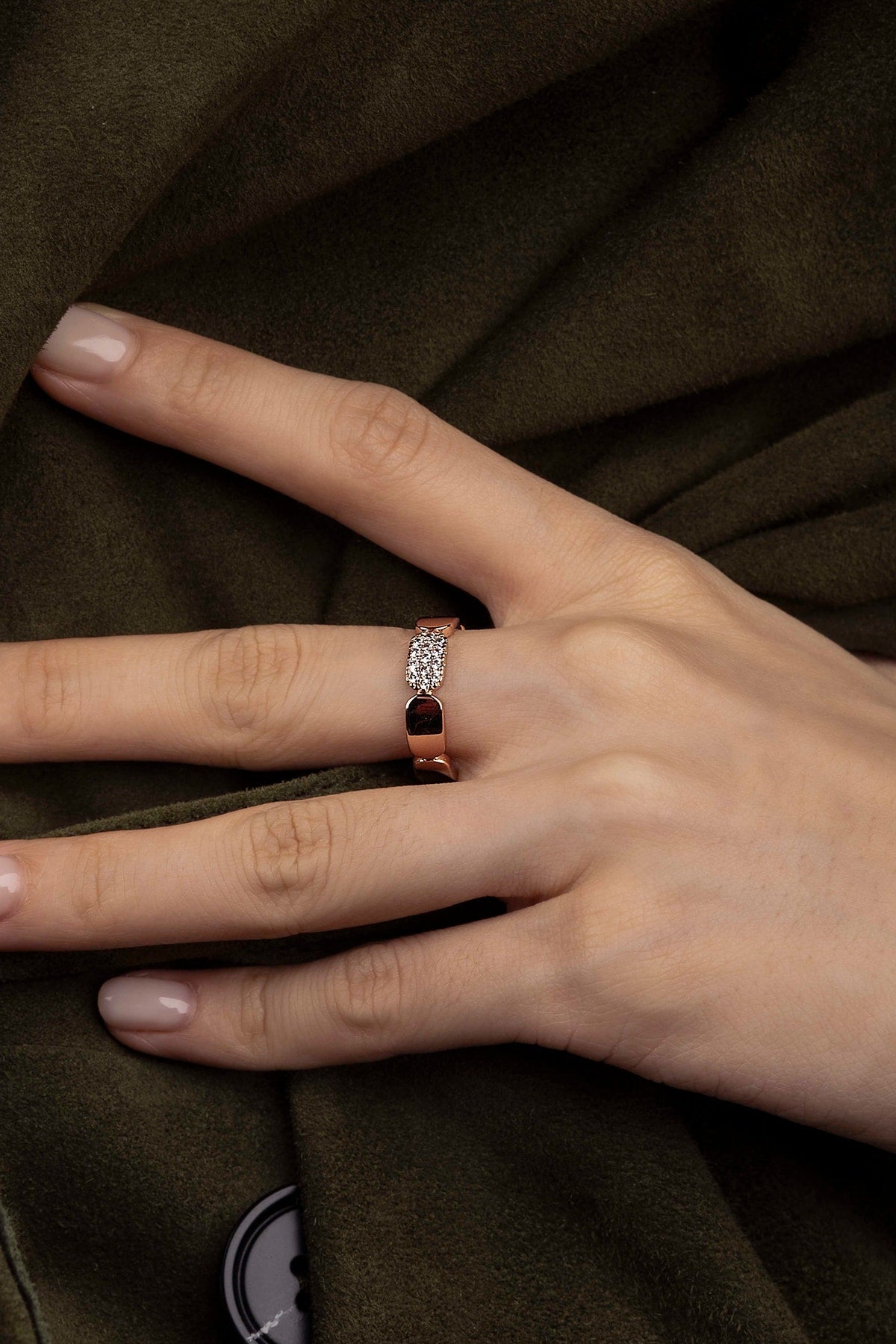 Hand wearing a ring with a diamond on a brown fabric background