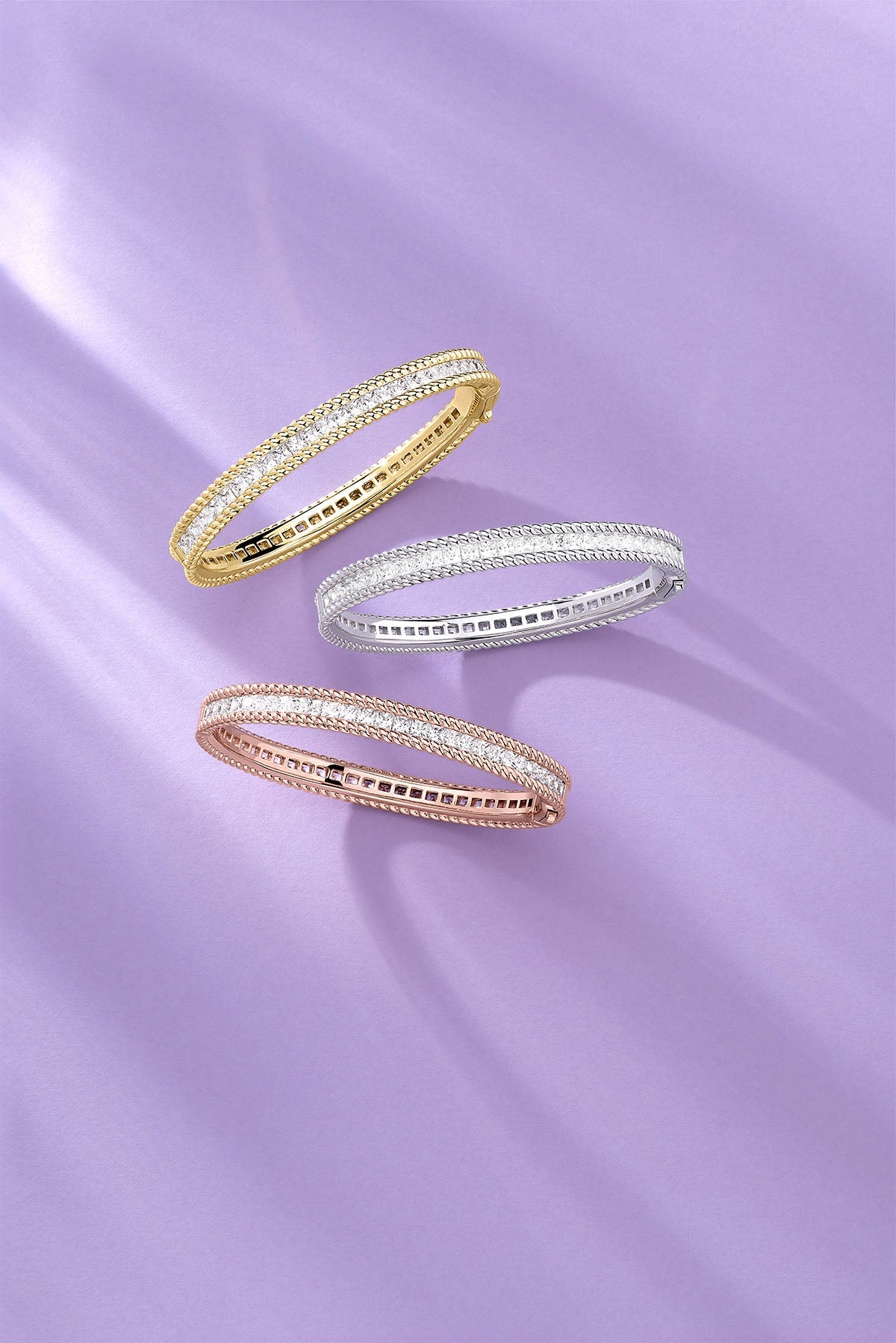 Three gold, silver, and rose gold rings on a purple fabric background