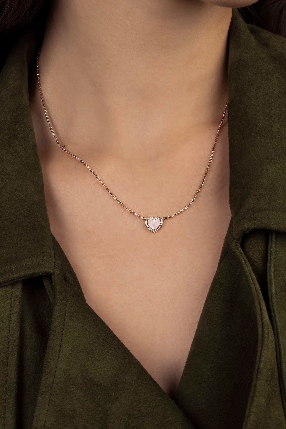 Rose gold necklace with a heart-shaped pendant worn by a person in a green shirt.