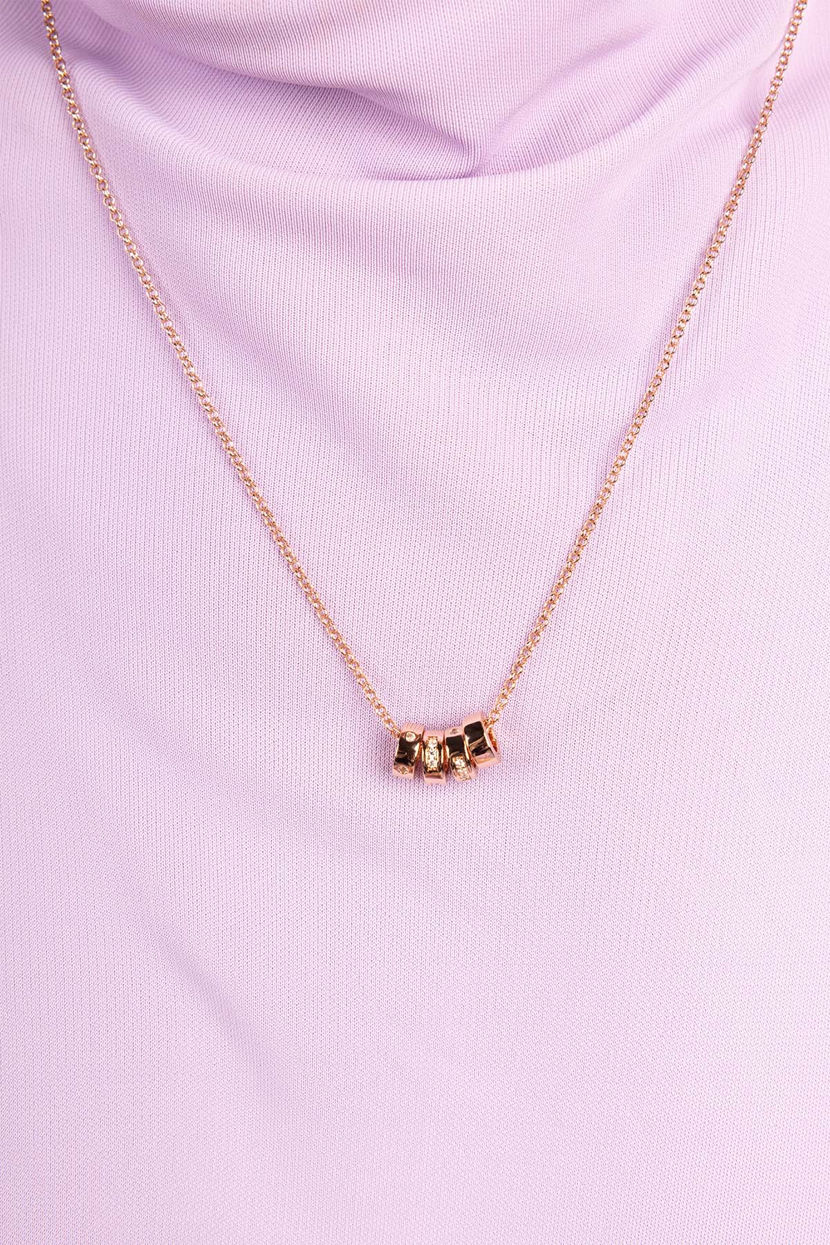 Gold necklace with a small pendant on a pink background