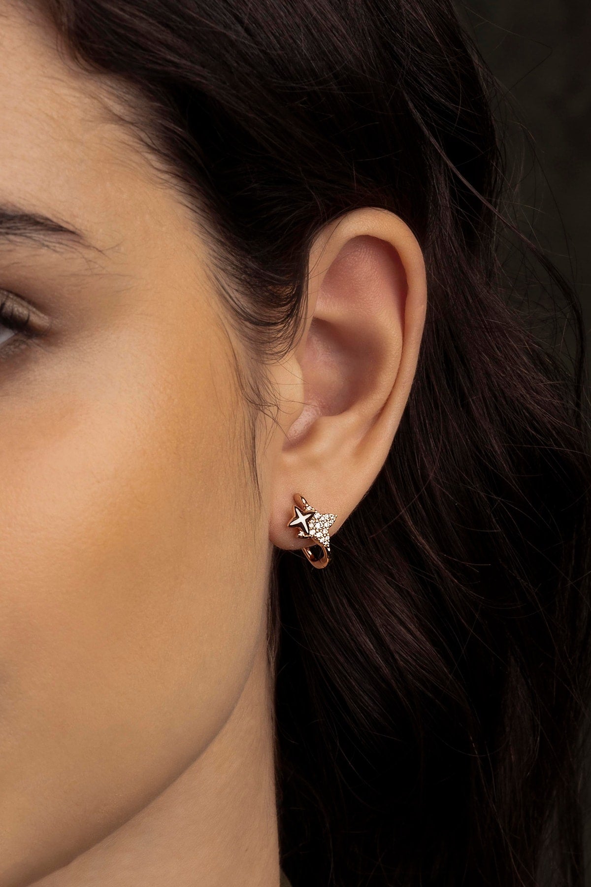 Close-up of an ear wearing a star-shaped earring with a dark background