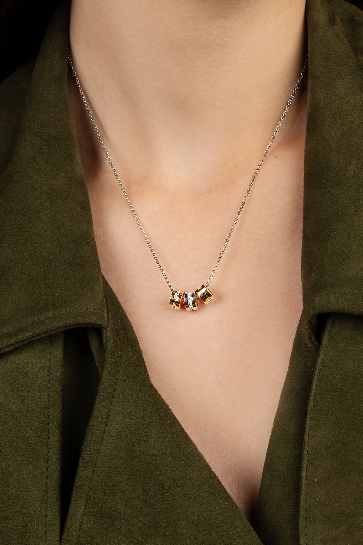 Necklace with three small pendants worn by a person in an olive green shirt.