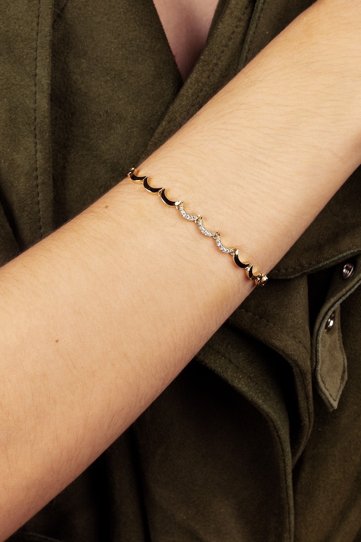 Close-up of a wrist wearing a delicate bracelet with a green jacket background
