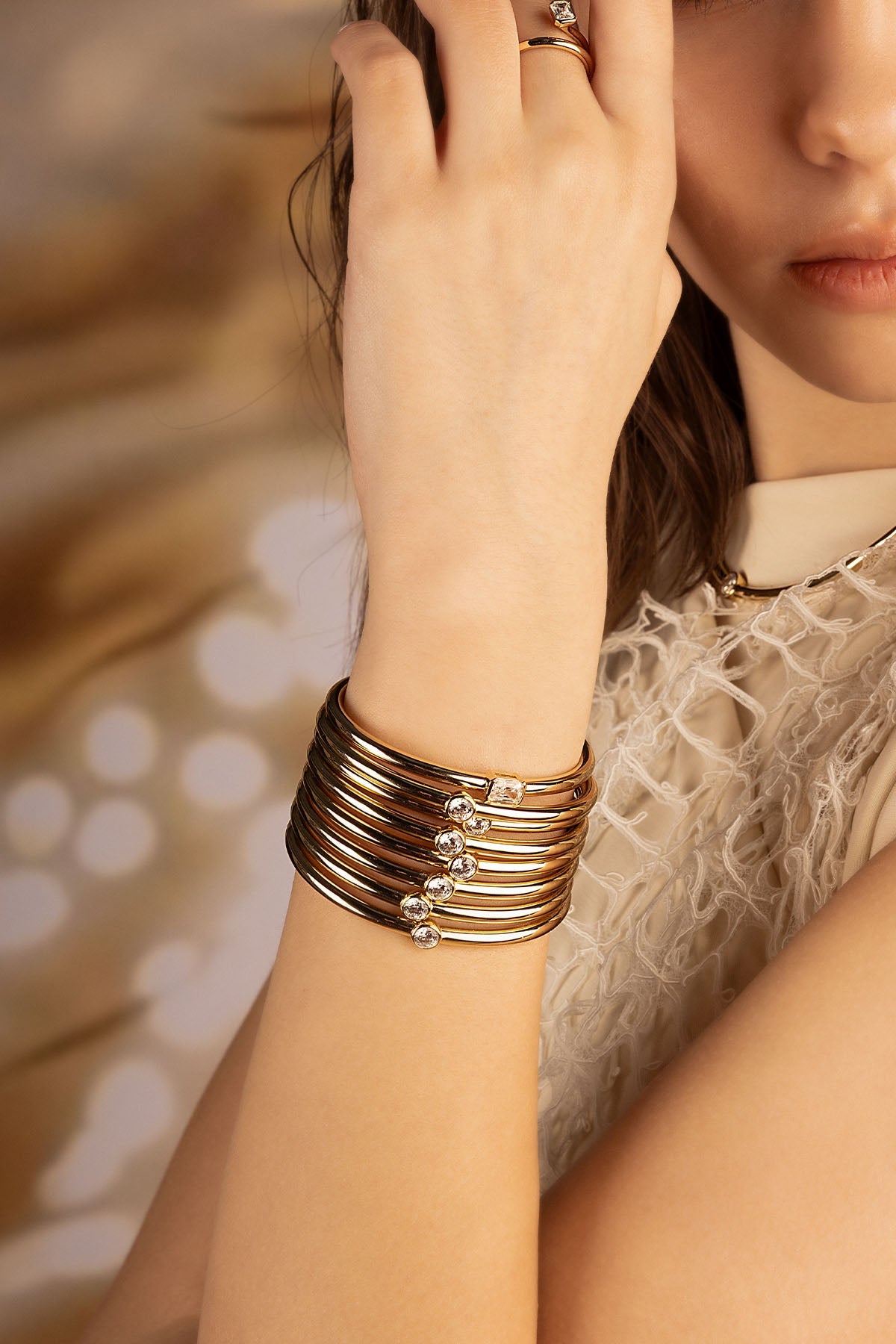 Bracelets APM Monaco: Yellow gold cuff-style layered bracelets with a ring on a model's hand.
