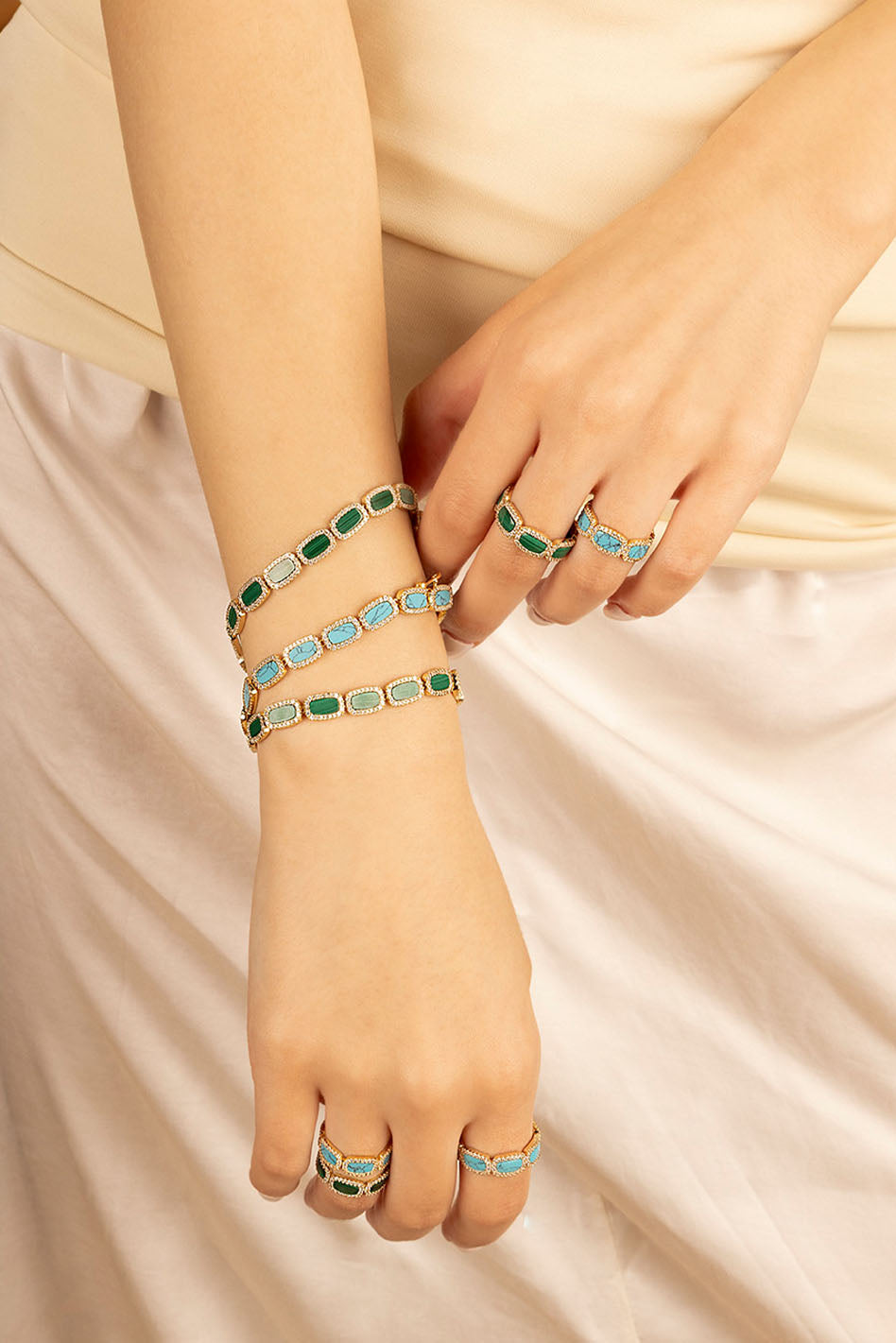 Bracelets APM Monaco with a gold-tone chain and stacked, alternating malachite-green and blue stones on the wrist.