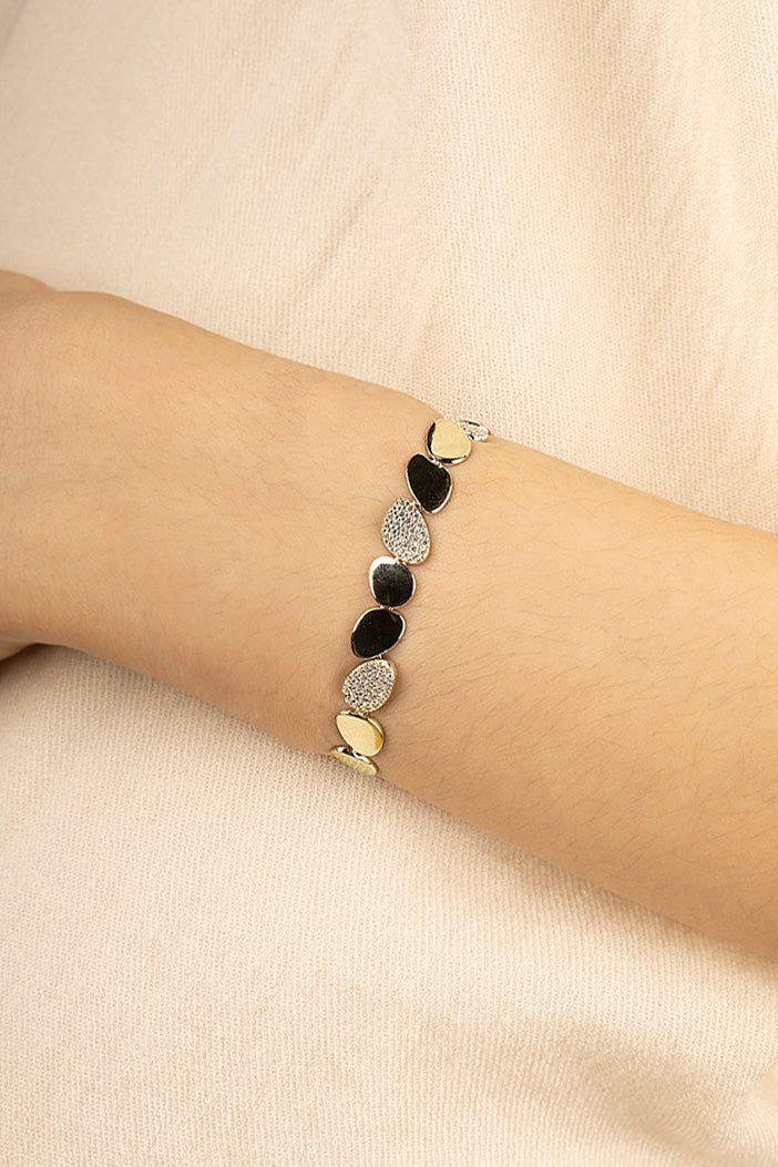 Bracelets APM Monaco galet bracelet featuring gold-tone and black accents with diamond pavé, worn on the left wrist.