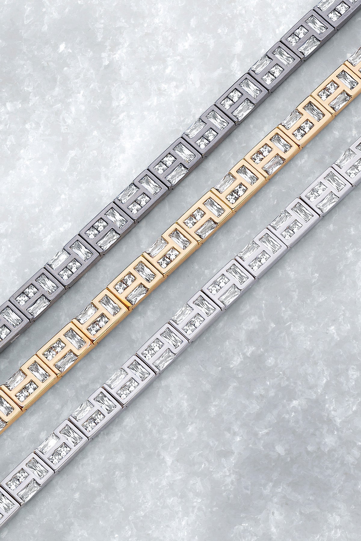 Three APM MONACO labyrinth bracelets in yellow gold, silver, and dark grey on a light white background