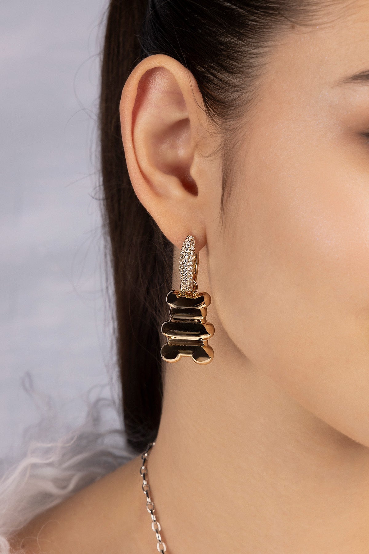 Close-up of a person wearing yellow gold hoop earrings with xl yummy bear design from APM MONACO against a neutral background