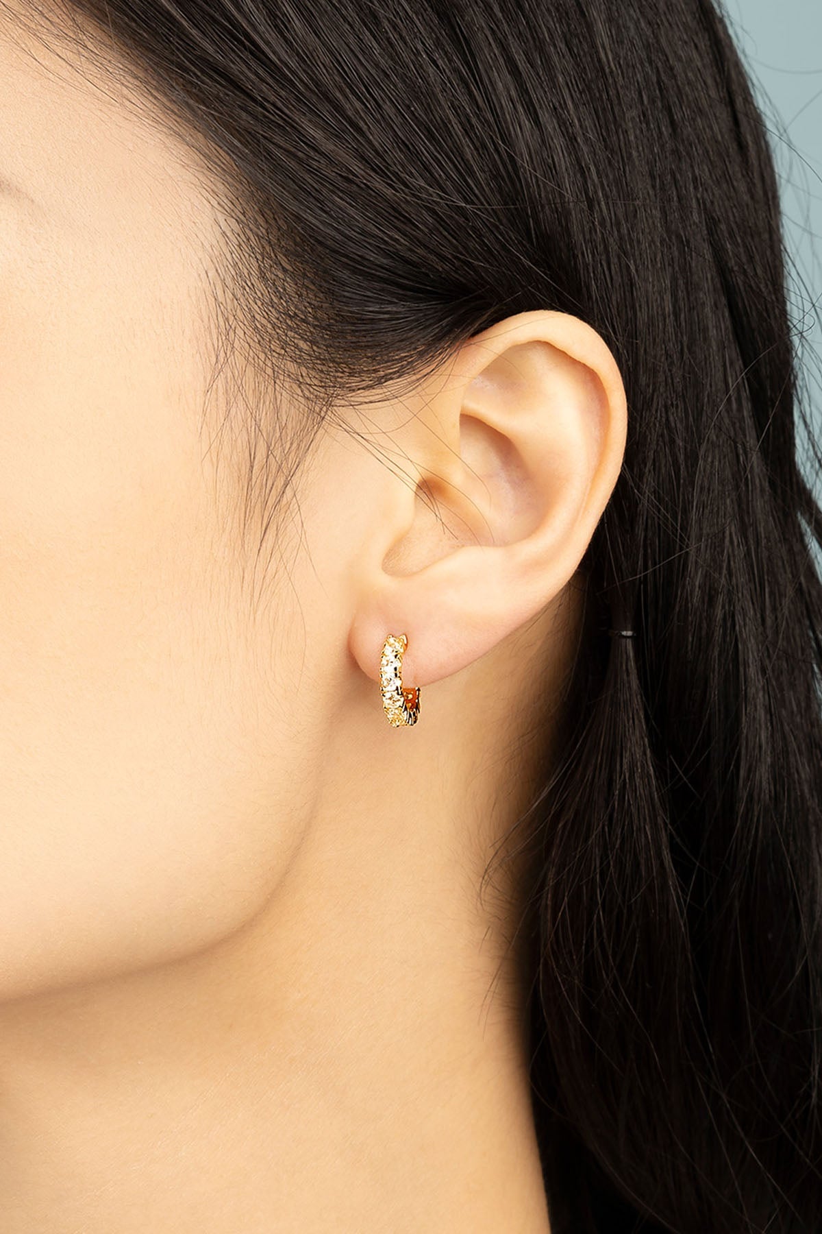 Earrings APM Monaco pavé huggie earrings in yellow gold with white pavé stones, worn on an ear.