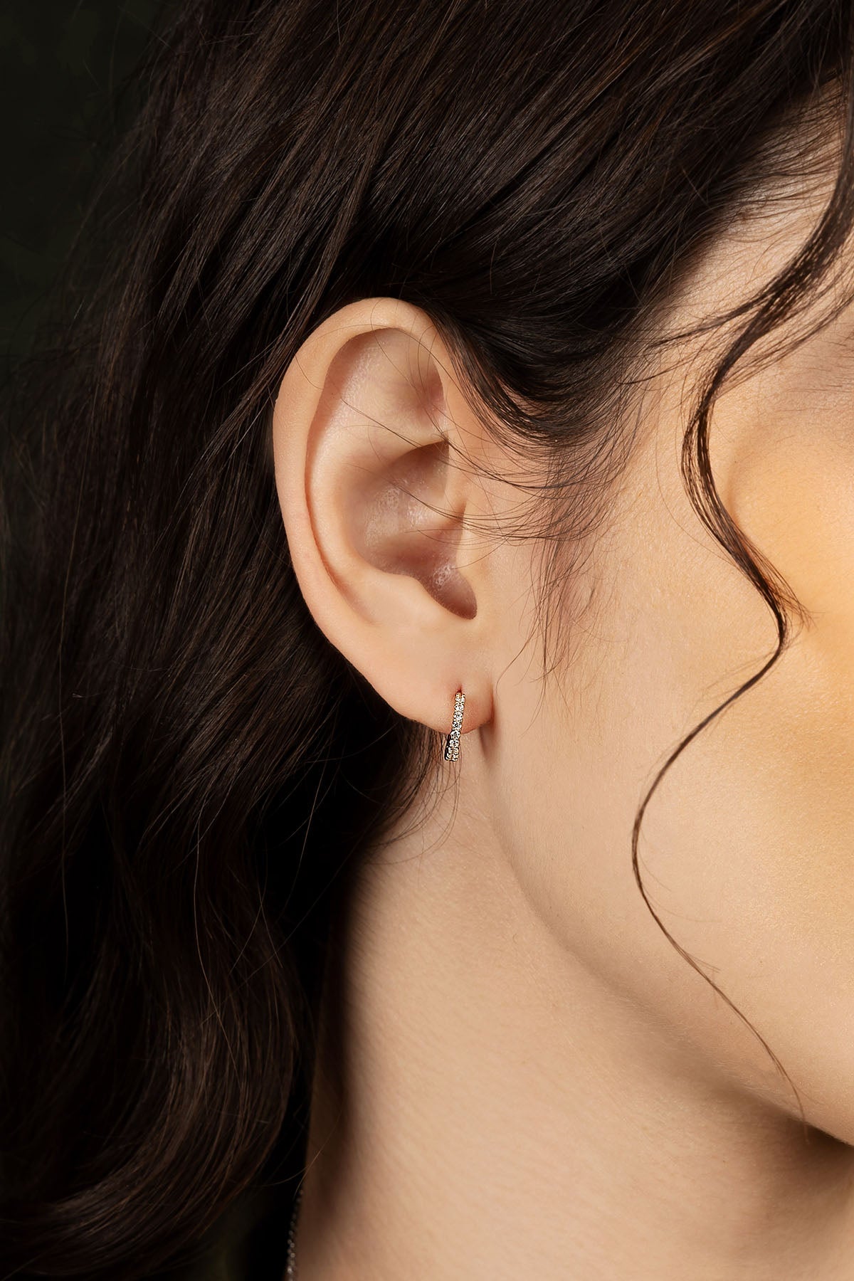 Close-up of an ear wearing earring with dark hair and skin.