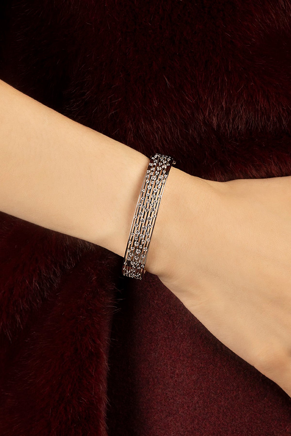 Woman wearing APM Monaco bracelet, layered shimmer against burgundy fur elegance.