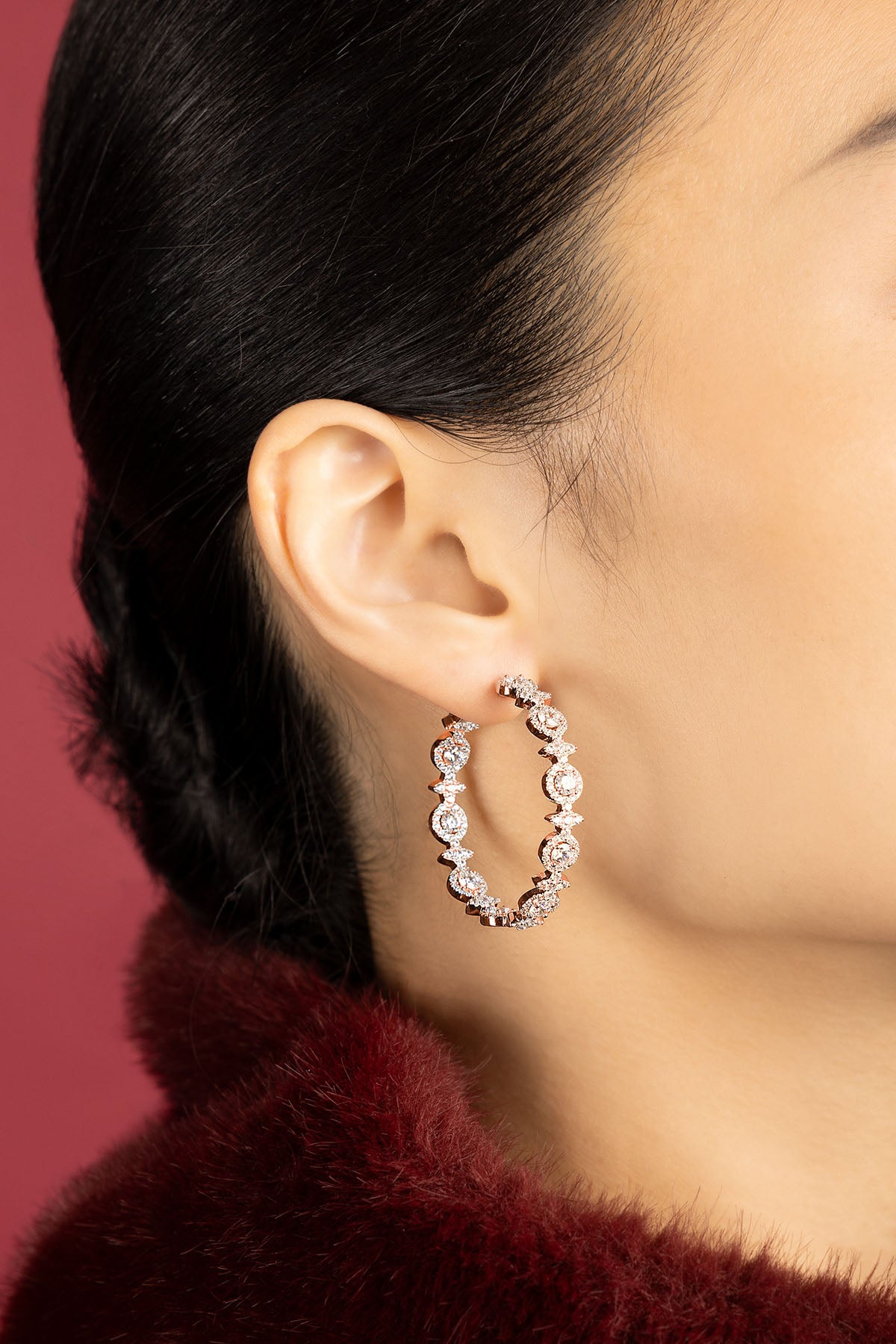 Woman wearing APM Hoop Earrings, a radiant rose glow against crimson elegance.