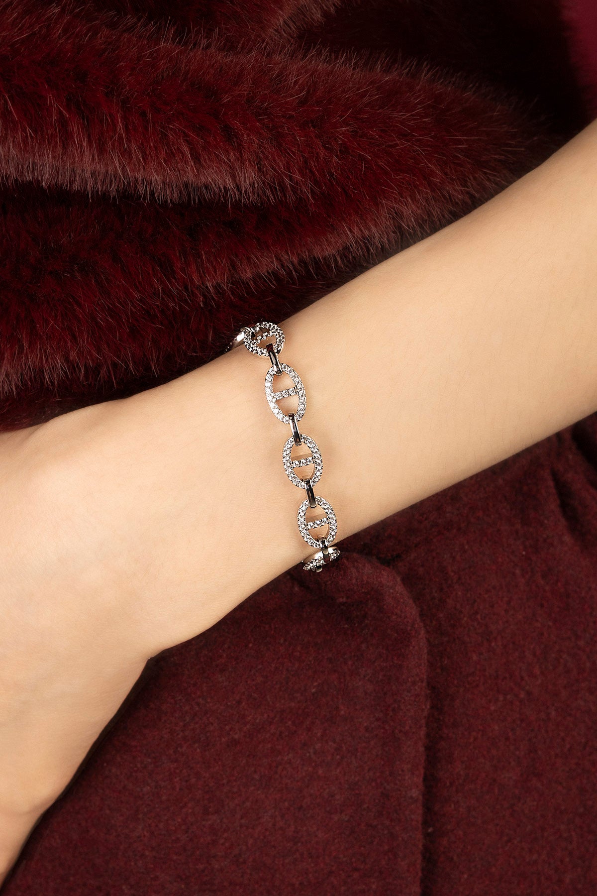 Woman wearing APM chain bracelet, a shimmering statement against rich burgundy.