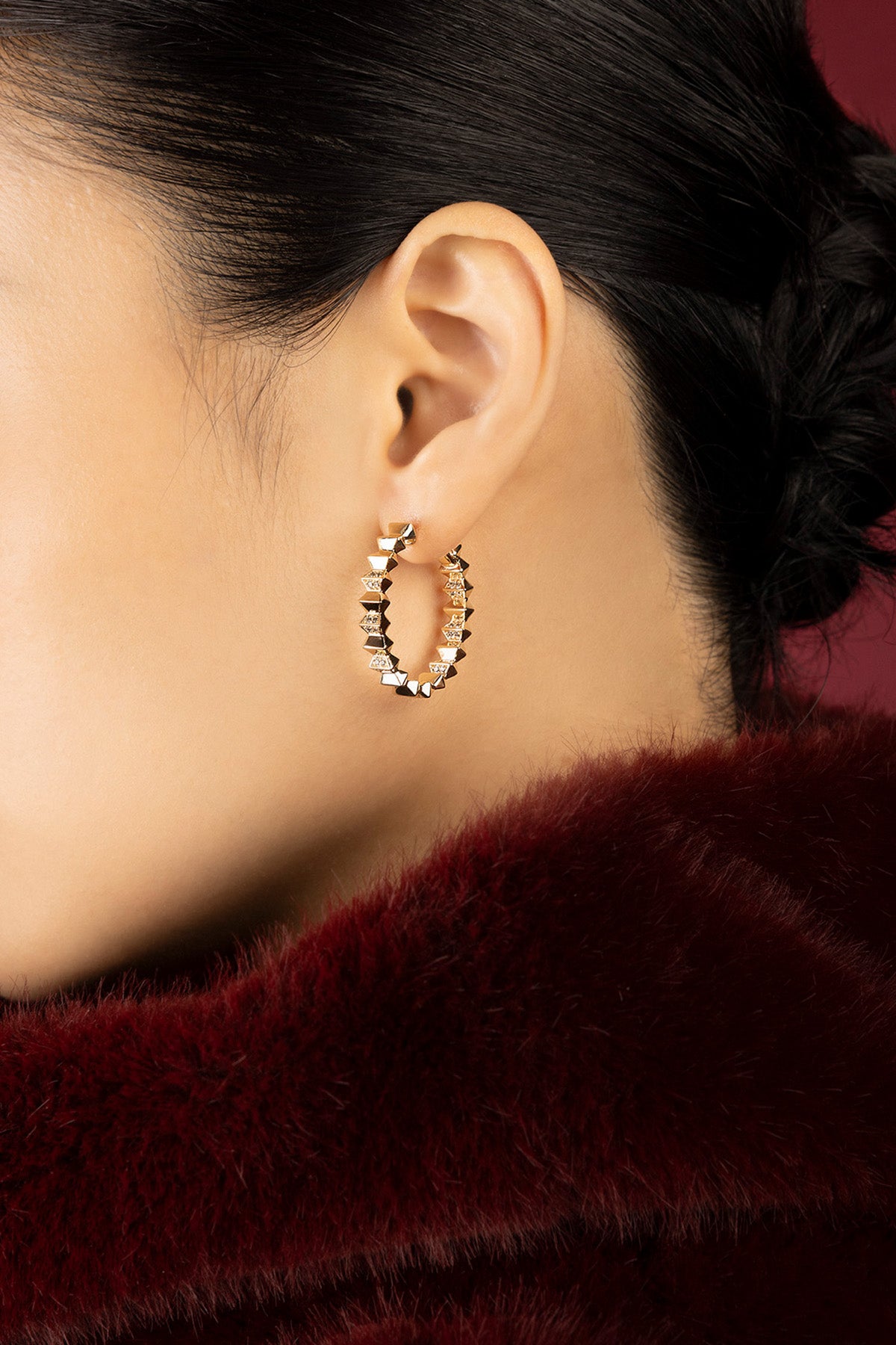 Woman wearing APM Monaco hoop earrings, bold spikes glowing against crimson elegance.