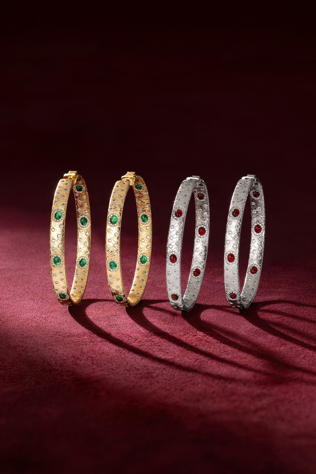 APM Bangles in golden and rhodium finish, glowing with emerald and ruby colors.