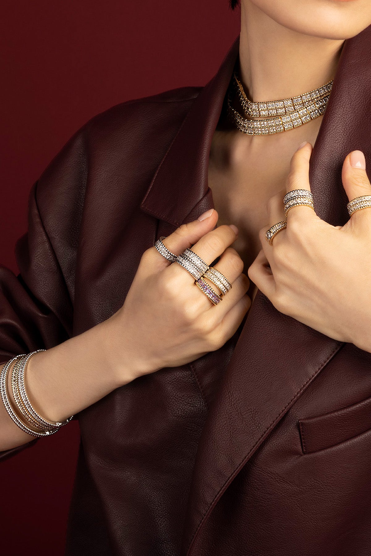 Woman wearing APM Monaco layered jewelry set, bold shimmer meets burgundy leather elegance.
