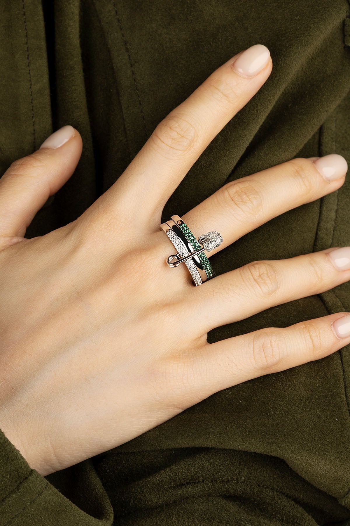 Close-up of a hand wearing multiple rings with green stones against a dark background