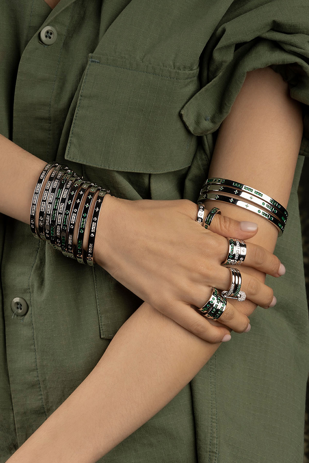 Close-up of a model wearing multiple bracelets and rings on a green background
