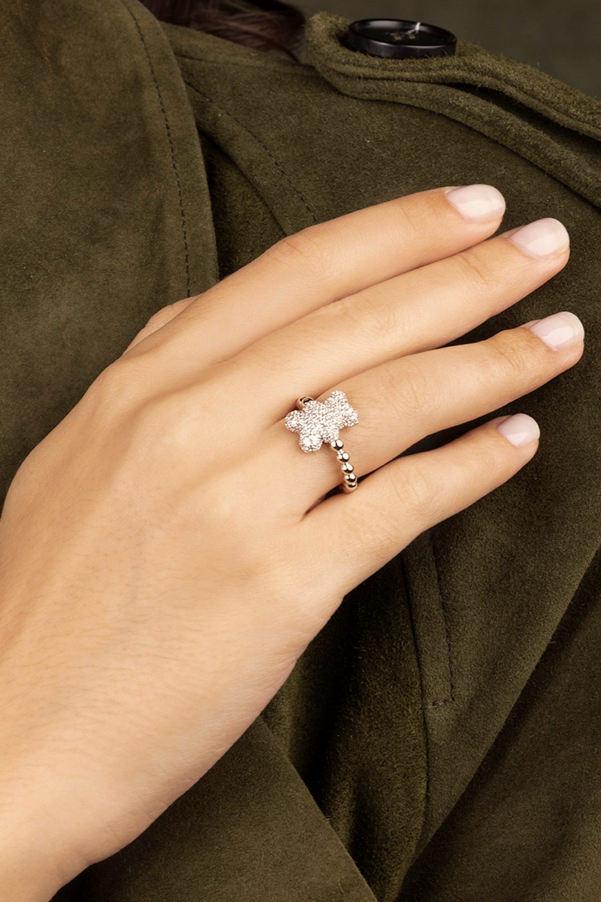 Hand wearing APM MONACO silver ring with yummy bear design on a green coat background