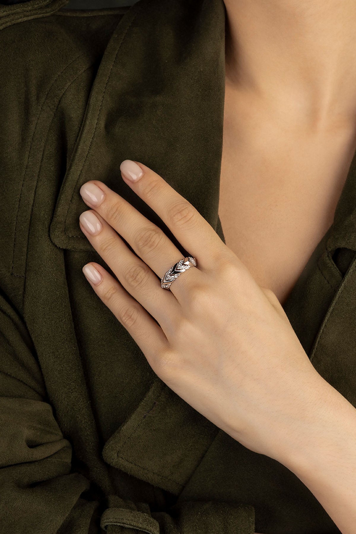 Close-up of a hand wearing a APM Monaco Kaa Ring in silver with a green coat in the background