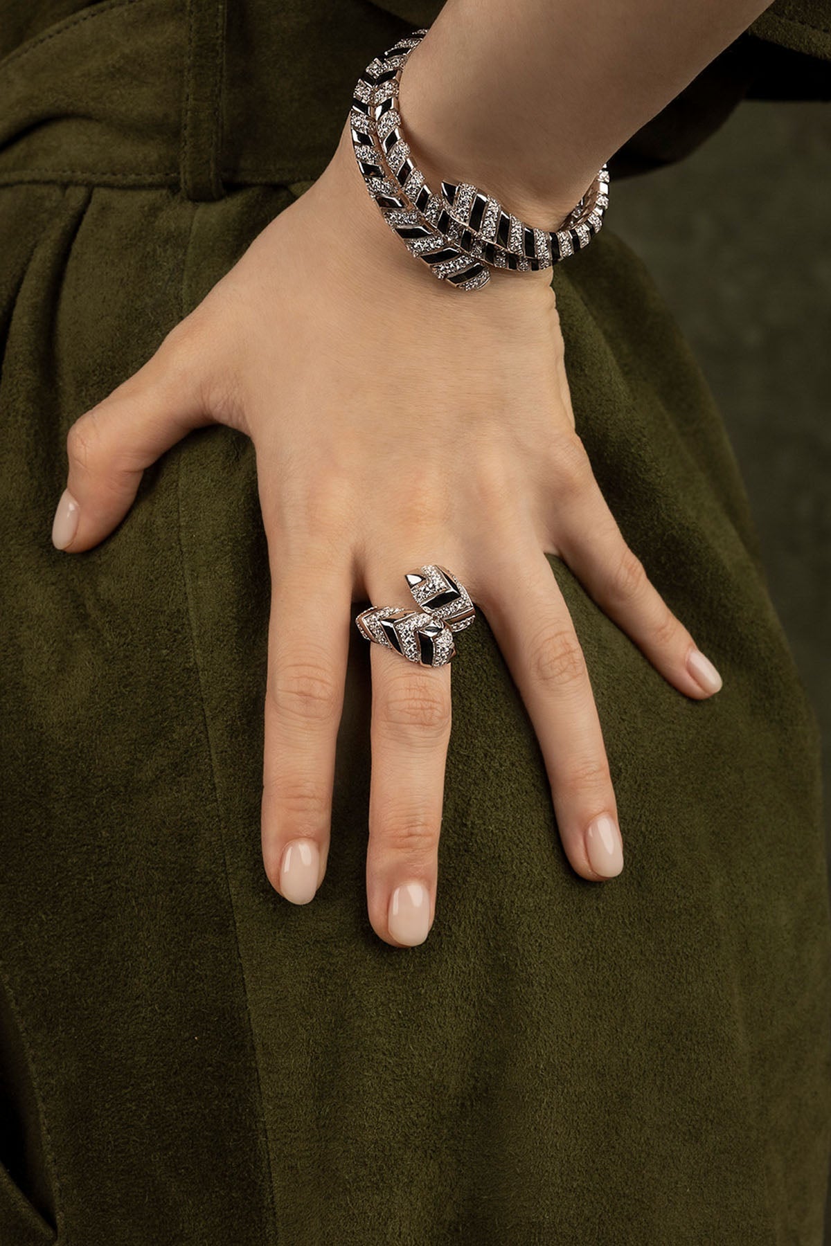 Hand wearing a silver bracelet and ring on a green fabric background