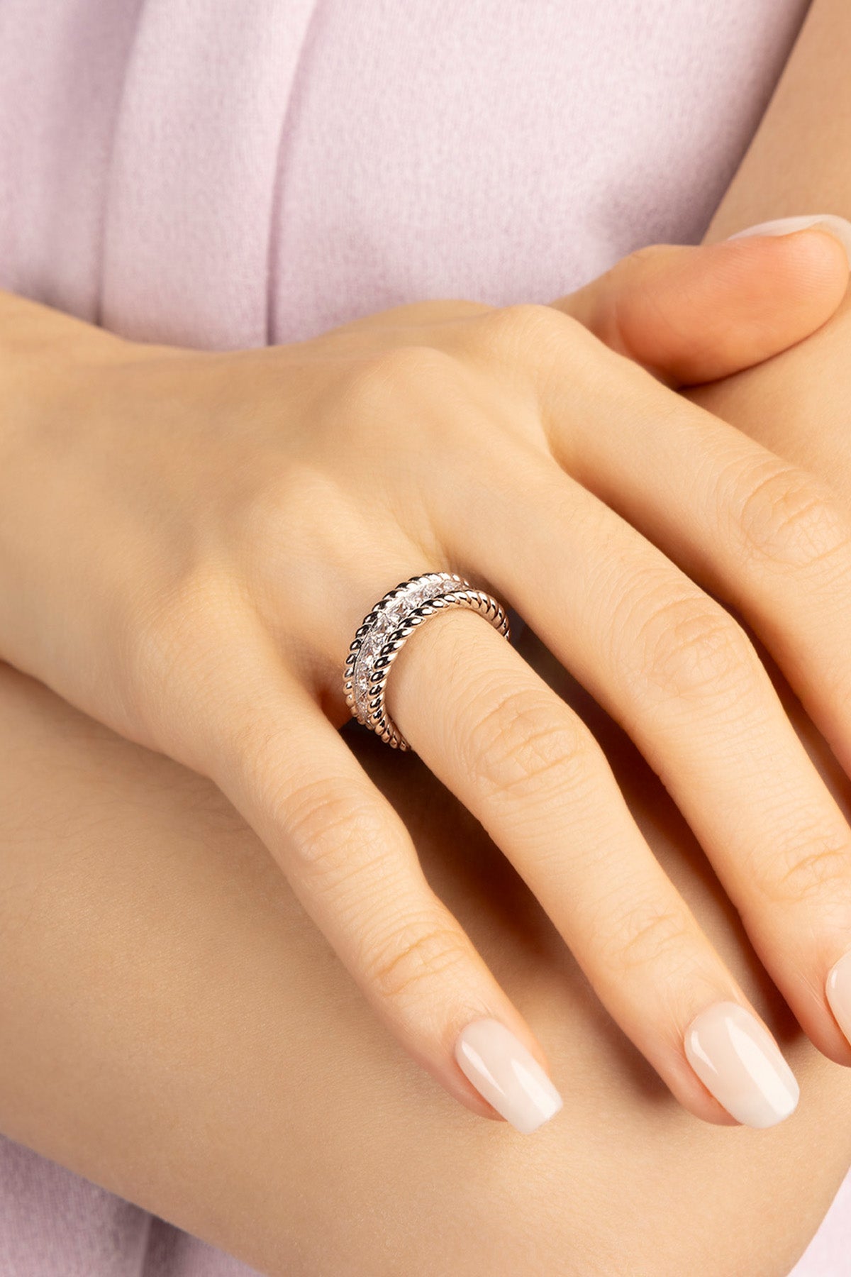 Close-up of a hand wearing a silver ring with a light background