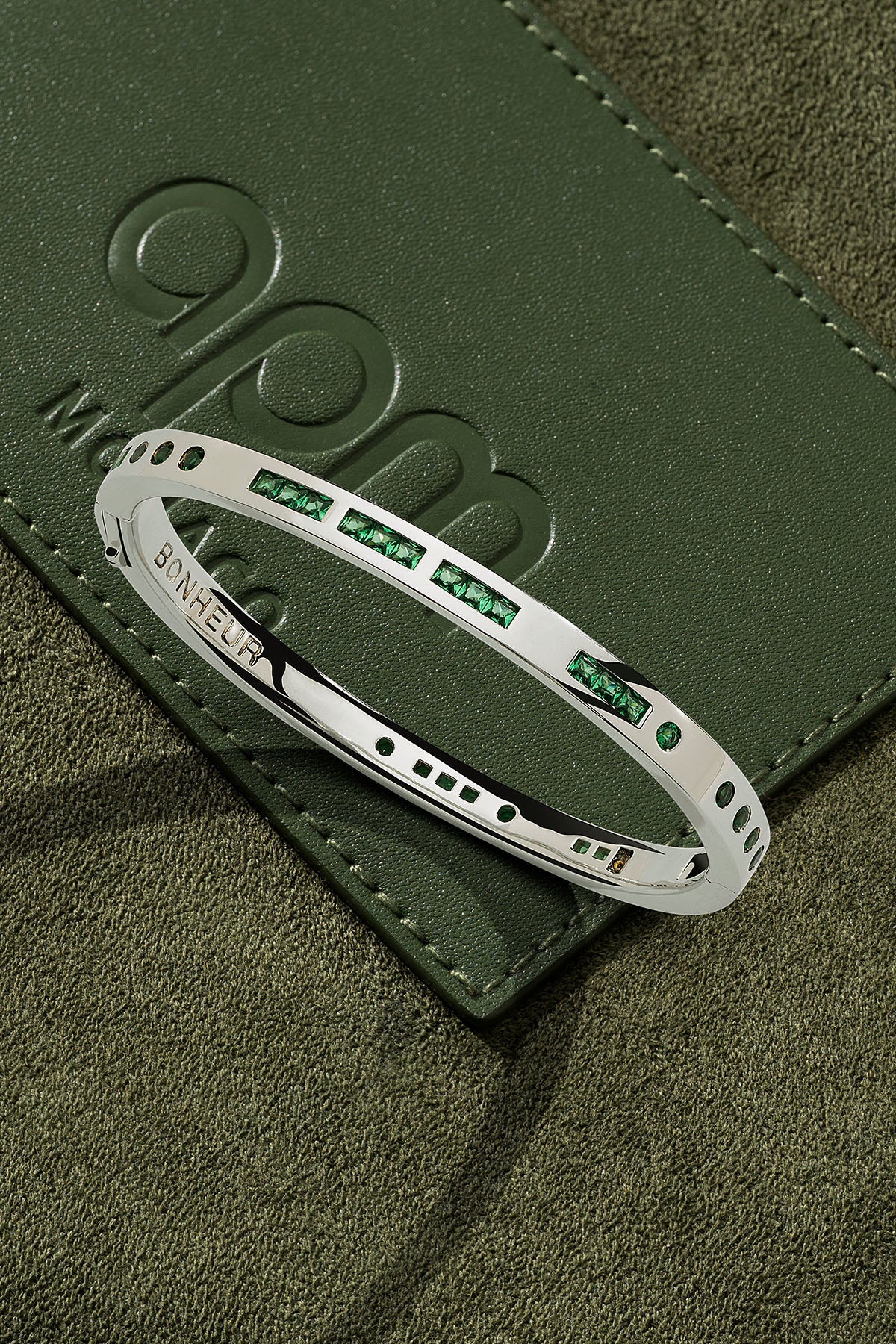 Silver bracelet with green stones on a green leather surface