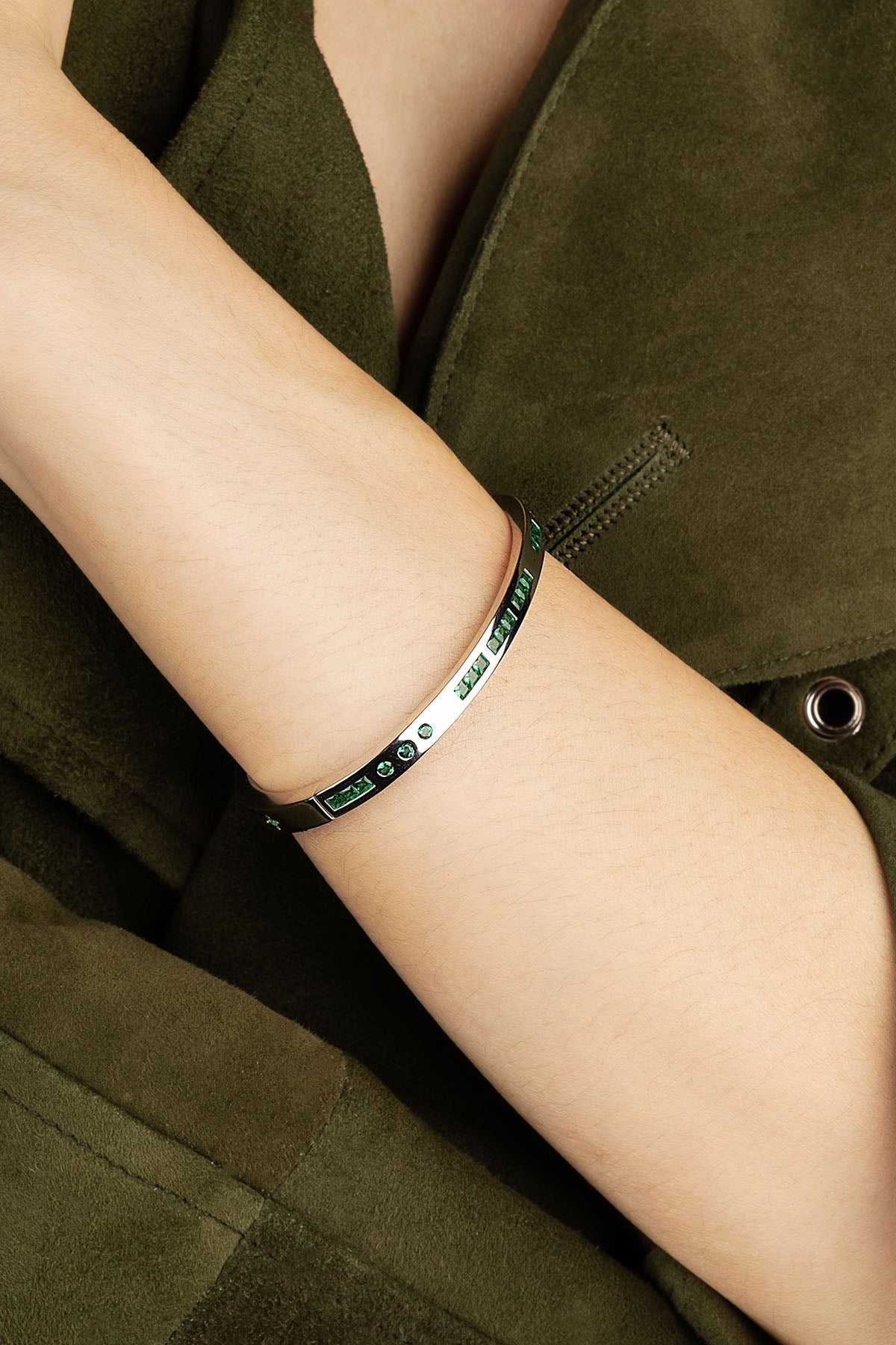 Silver bracelet with green stones on a person's wrist against a green jacket background