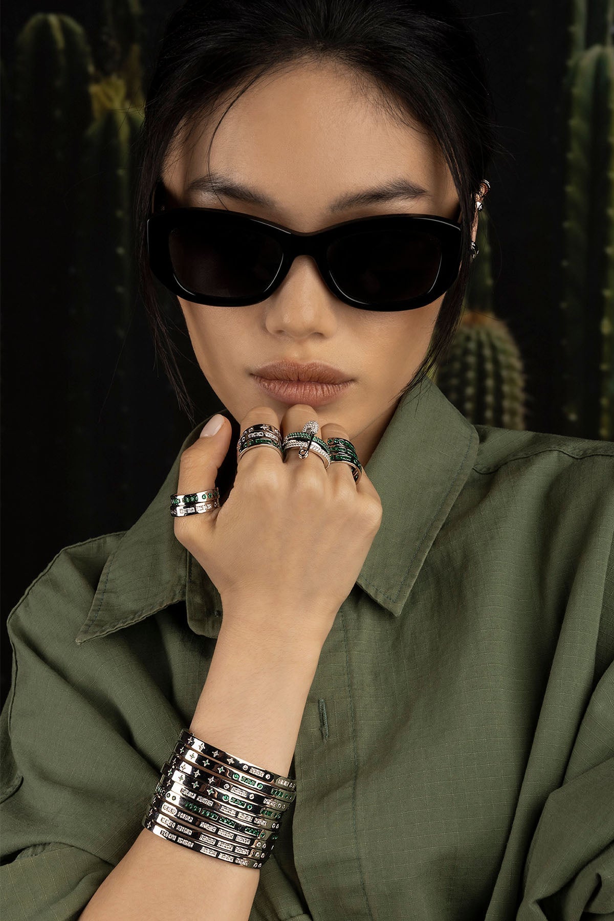 Person wearing sunglasses and multiple rings with a cactus background
