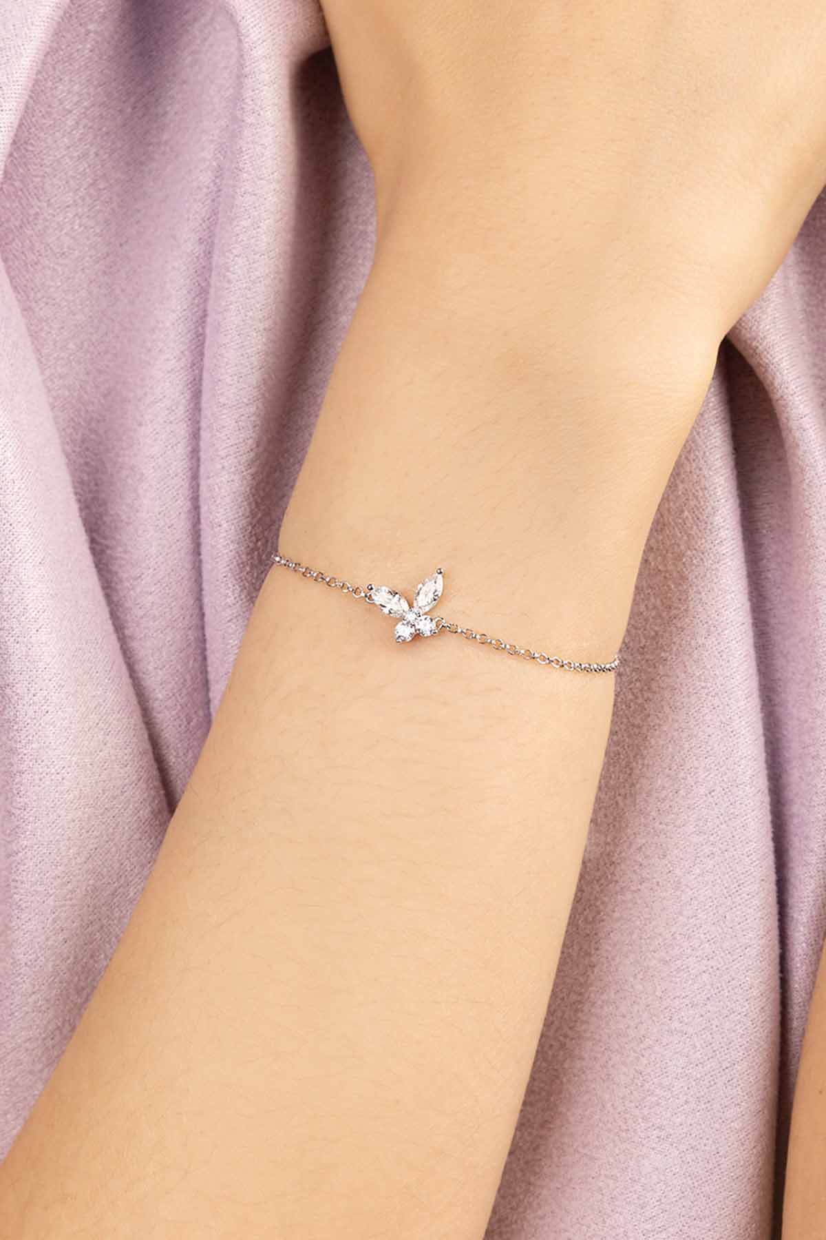 Silver-tone bracelet with a butterfly-shaped clasp on a wrist against a soft pink fabric background