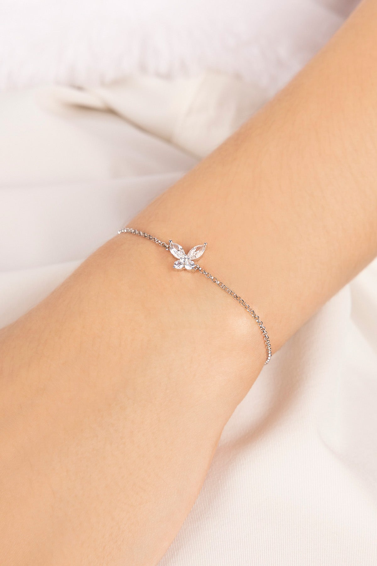 Silver bracelet with a butterfly on a wrist against a light background