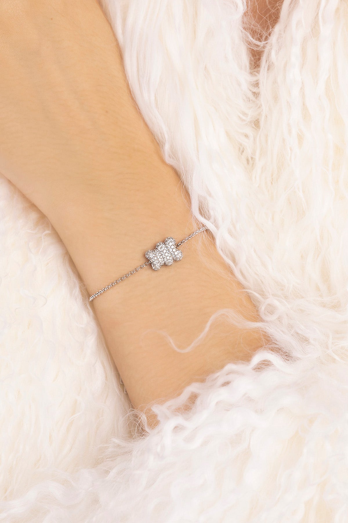 APM MONACO silver bracelet with baby mood yummy bear design on a wrist against a white fur background