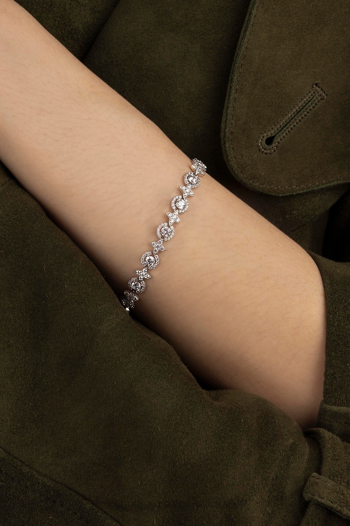 Silver bracelet on a person's wrist with a dark green coat background