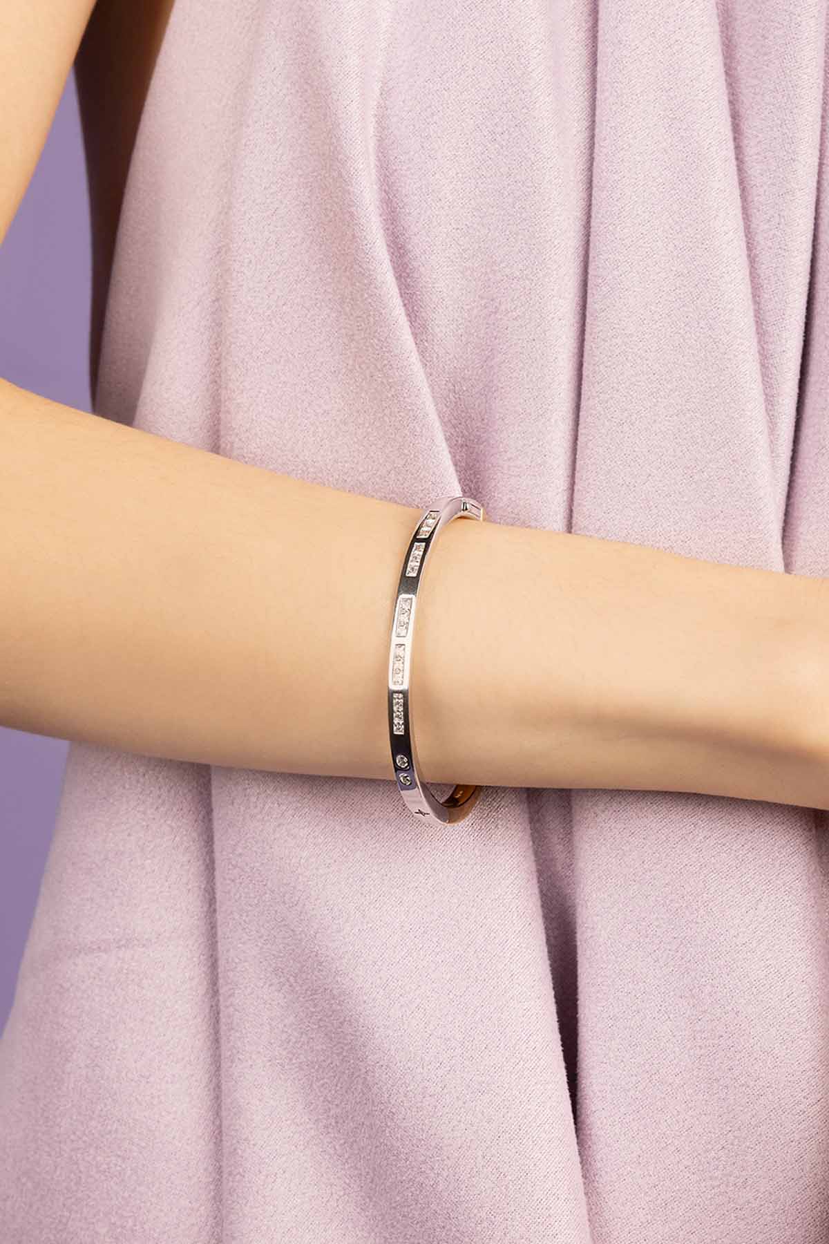 Silver bracelet on a person's wrist with a soft pink fabric background