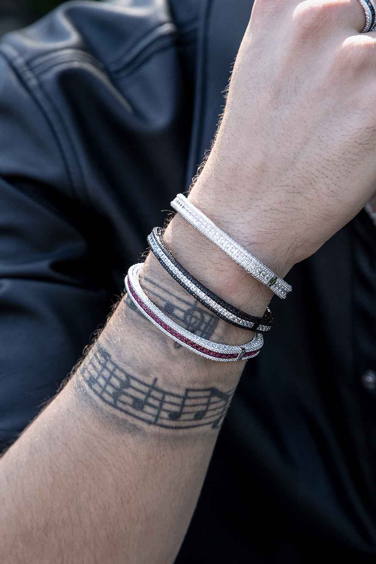 Bracelets APM Monaco, pavé bangles on a forearm with multicolor stones. three stacked gemstone bangles, metal setting, shimmering stones.