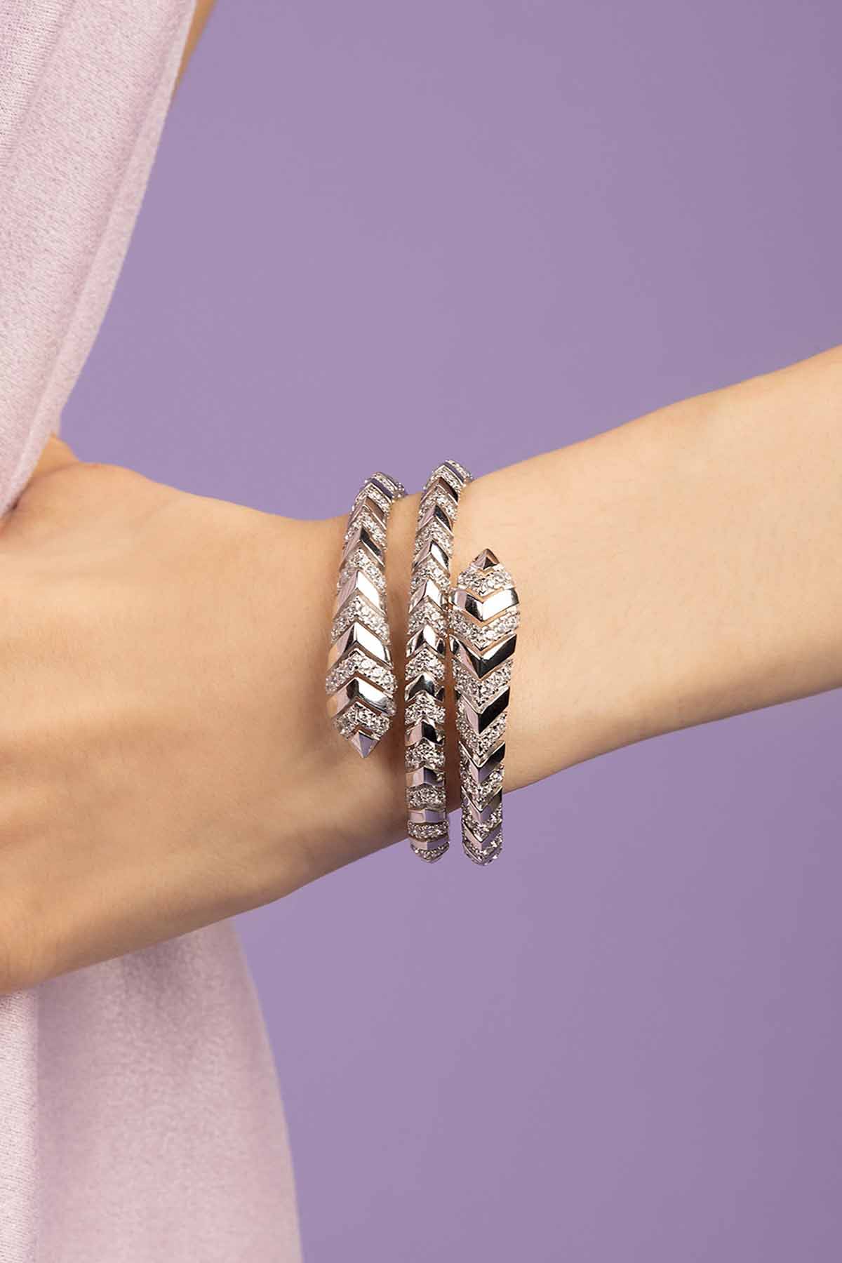 Silver bracelets on a wrist against a purple background