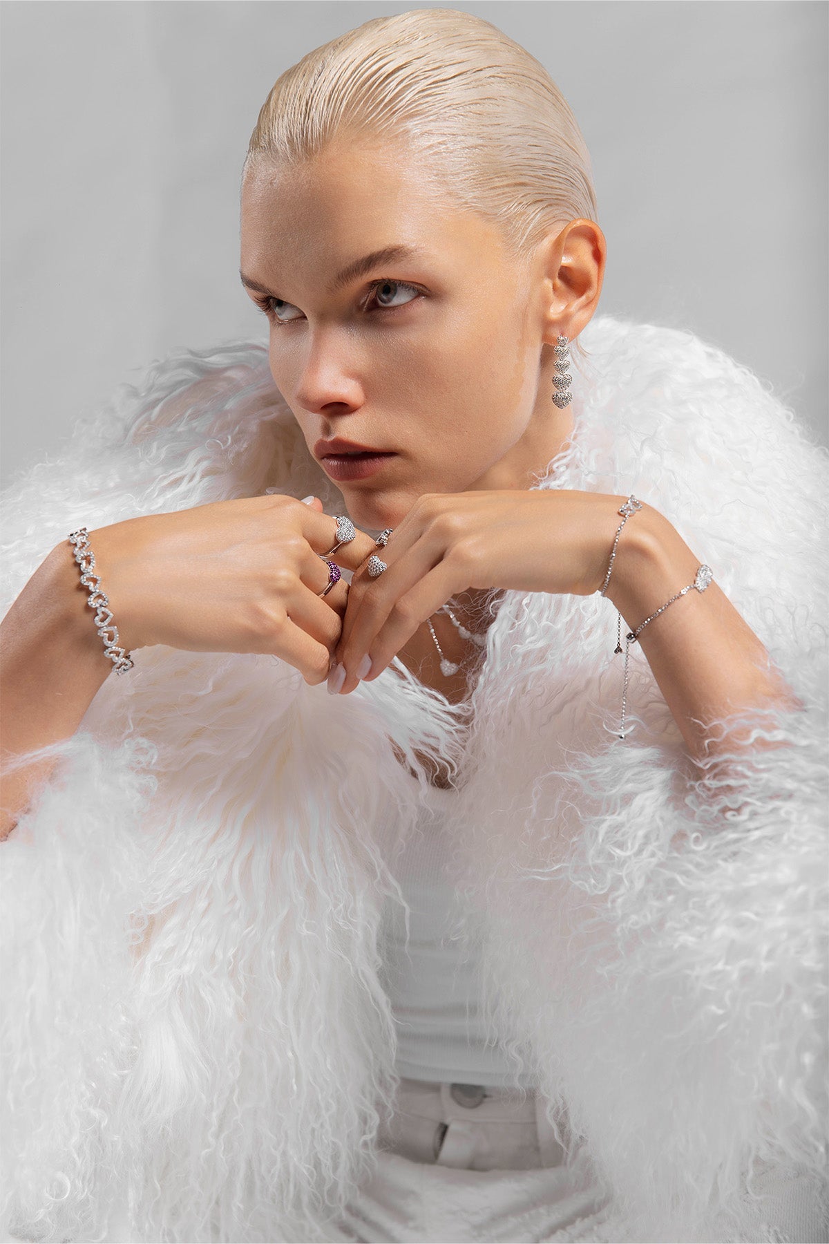 Model wearing a white feathered coat and with APM MONACO heart-shaped adjustable jewelry against a gray background