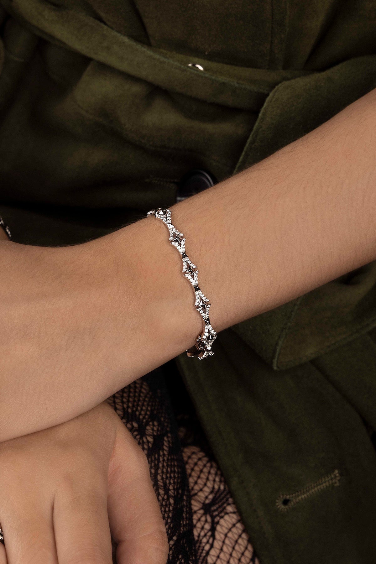Silver bracelet on a wrist with a dark green jacket background