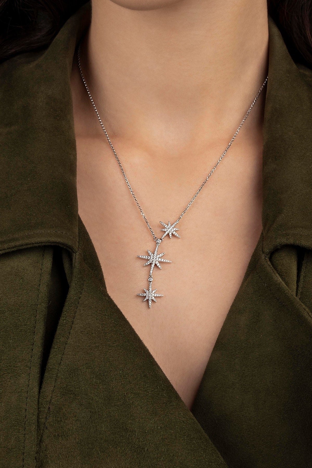 Silver necklace with star-shaped pendants worn by a person in a green outfit.