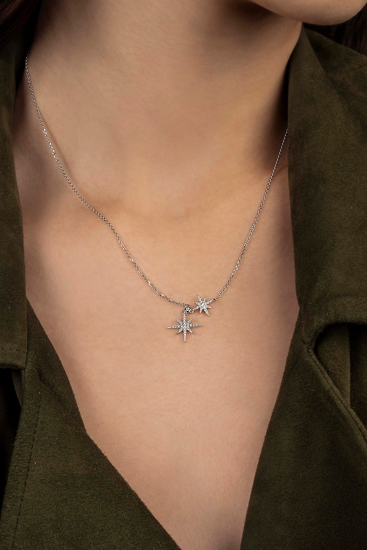 Silver necklace with star pendants worn by a person in an olive green shirt.