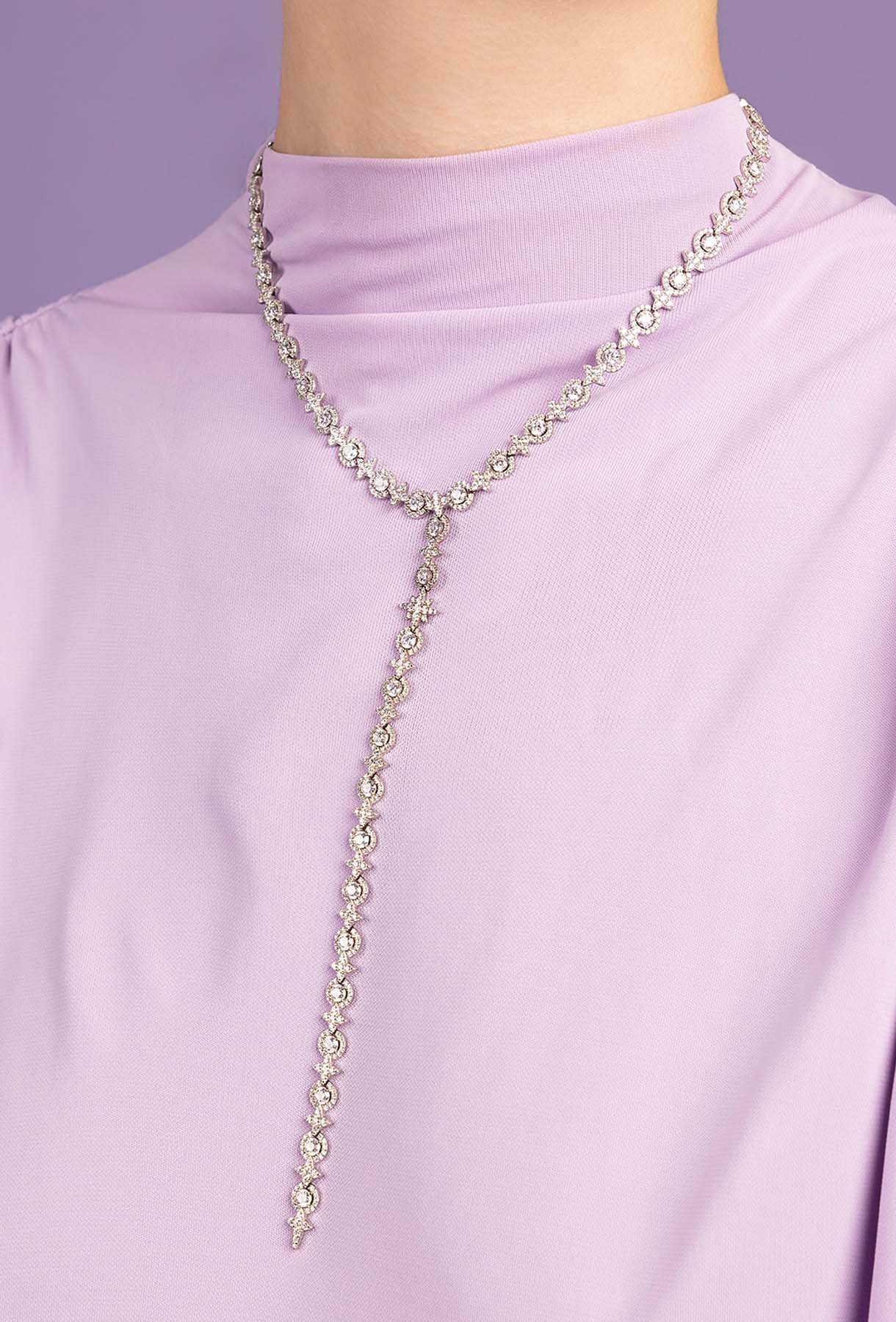 Silver-tone chain necklace on a person wearing a light purple top against a light purple background